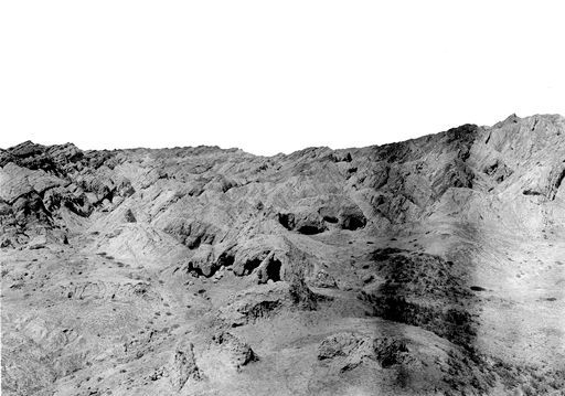 B 1168: Panorama einer Hügellandschaft mit Höhlenanlage im westlichen Zentrum des Tals, im Vordergrund eine Stūpa-Ruine
