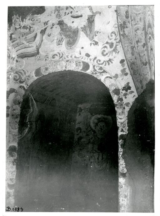 B1183: Blick auf eine Kultbildwand: links neben der Mandorla des Buddha wird der Eingang in den linken Gang mit einer Blütenbordüre geschmückt, darüber befinden sich Streublüten und Wolken. Im Gang sind stehende Buddhas und Bodhisattvas sichtbar. (B_1183_IB_9205_8822_8832_9071_Kum_pos.jpg)