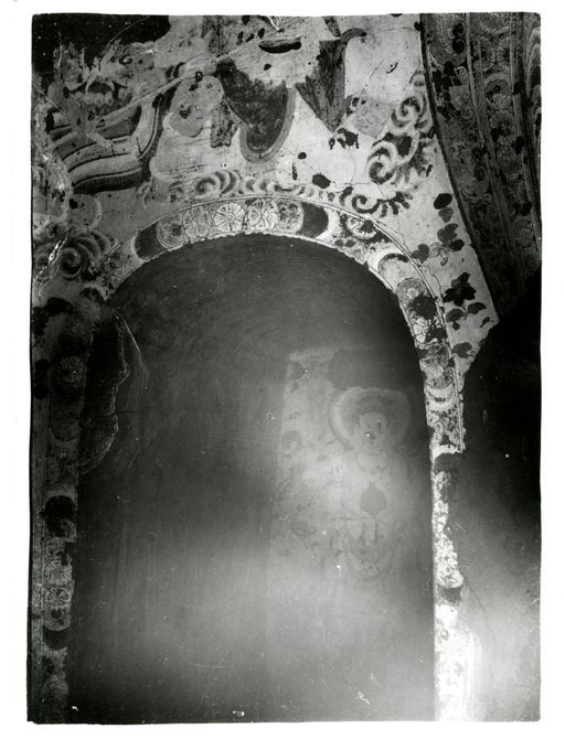 B 1183: Blick auf eine Kultbildwand: links neben der Mandorla des Buddha wird der Eingang in den linken Gang mit einer Blütenbordüre geschmückt, darüber befinden sich Streublüten und Wolken. Im Gang sind stehende Buddhas und Bodhisattvas sichtbar.