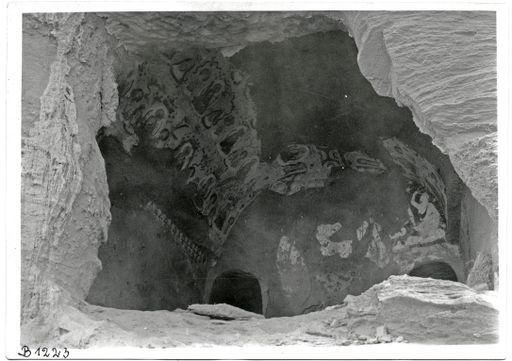 B 1223: Innenansicht einer Zentralpfeilerhöhle mit Wandmalereien: Reihen von sitzenden lehrenden Buddhas und Nimbus vor Mandorla zwischen den Eingängen zum Umwandlungsgang