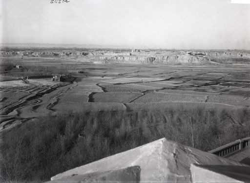 B 1232: Blick von einem Dachgiebel: mit Feldern, kleinem Begräbnisplatz und einem Plateau mit Häusern bis zum Gebirge.