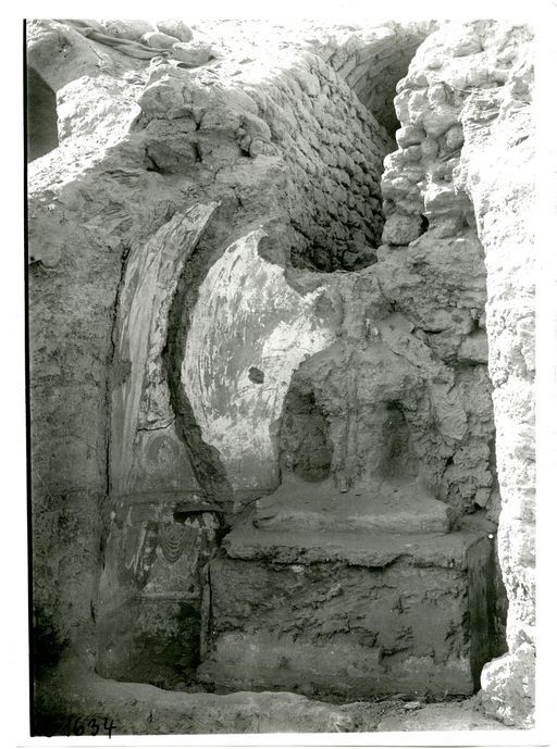 B 1634: Lehmplastik einer sitzenden Buddhafigur mit Resten von Wandmalerei in einer kleinen Cella vor einem gemauerten Stollen, der uighurische Manuskripte und künstliche Blumen enthielt.