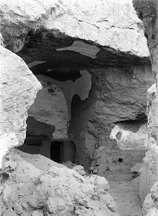 B1674: Cella einer Höhle mit Tonnengewölbe und Umwandlungsgang, geweißte Verputzreste. Blick durch zerstörte Front von links. Rechts zeigt sich ein ähnlicher Nebenraum wie links. Junge lehnt an der rechten Wand. (B_1674_Bez_10-13.jpg)