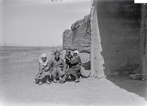 B 1696: Familie mit Kind sitzt am Eingang einer hohen Ziegelmauer (Rasthaus-Mauer?)