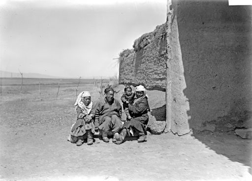 B 1697: Familie mit Kind sitzt am Eingang einer hohen Ziegelmauer (Rasthaus-Mauer?)