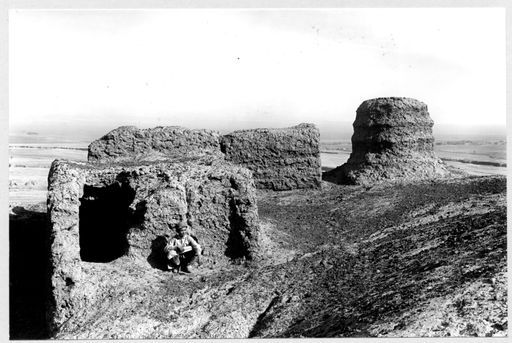 B 1704: Ein Junge hockt neben Resten von Bauten und Stūpastumpf auf Hügelkuppe.