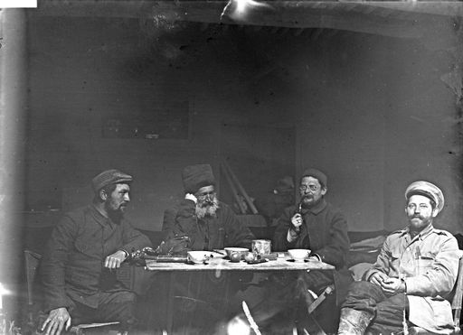 B 1878: Die Grabungsmannschaft Turfan III: Hermann Pohrt, Albert Grünwedel und der russische Reisende M.M. Berezofskij, Theodor Bartus. Das Ambiente und die Notizbücher auf dem Tisch deuten auf eine Fachbesprechung in ihrem Quartier, ausgerüstet mit Klappmöbeln.