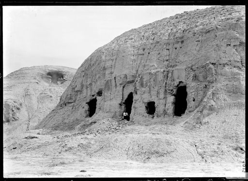 B804: a) Grünwedel sitzt im Eingang einer Kulthöhle. Über ihm sieht man Reste vom Lehmskulpturen. Im Hintergrund sind Arbeiter beim Leeren von Höhle 9. (B_804_Sho_6-9.jpg)