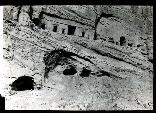 T 100: Westlichen Wand der großen Schlucht mit einer Reihe von Höhlenräumen, die in alter Zeit nur über eine hölzerne Galerie und Treppen zu erreichen waren. Einkerbungen für die Holzkonstruktionen sind deutlich sichtbar. Bei den großen Hohlräumen wurde eine bemalte hölzerne Asche-Urne gefunden, die sich heute im Museum in Berlin befindet.