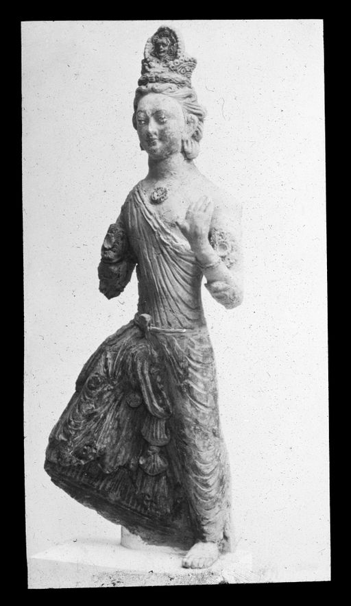 T 617: Statuette einer stehenden Devatā mit Krone, die eine antike Maske (?) (Sonne oder Schlange?) im Vorderstück hat