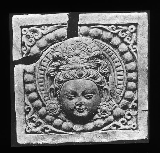 T 678: Gebrochene Reliefplatte mit Kopf einer Gottheit mit hohem Haaraufbau im Perlkranz